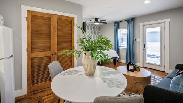 Un salon moderne avec une table à manger ronde, un canapé, un ventilateur de plafond et une grande fenêtre avec des rideaux.
