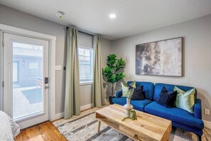 Een woonkamer met een blauwe bank, een houten salontafel, een plant in pot en een schilderij aan de muur.