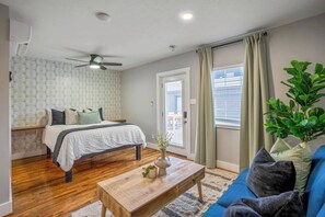 Een slaapkamer met een bed, een plafondventilator, een houten vloer, een raam met gordijnen en een potplant.