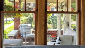 A room with a large window, a grey sofa, and a brick wall. - Experience Coast Guard Festival Like a Local in a Charming Downtown Cottage (Grand Haven)