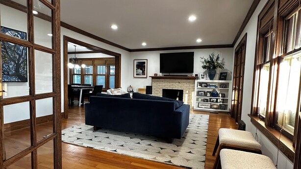 A spacious living room with a dark blue sofa, wooden flooring, a fireplace, and a television mounted on the wall. - Experience Coast Guard Festival Like a Local in a Charming Downtown Cottage (Grand Haven)