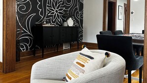 A modern living room with a black and white patterned wall, a dark wooden dining table, and a grey sofa with patterned cushions. - Experience Coast Guard Festival Like a Local in a Charming Downtown Cottage (Grand Haven)