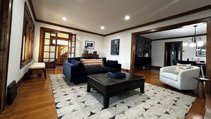 A spacious living room with a dark blue sofa, a white armchair, and a black coffee table. - Experience Coast Guard Festival Like a Local in a Charming Downtown Cottage (Grand Haven)