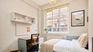 Een slaapkamer met een bed, bureau, stoel, planken en een raam met uitzicht.