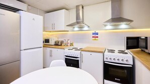 Een keuken met witte kastjes, een fornuis, een magnetron en een koelkast.