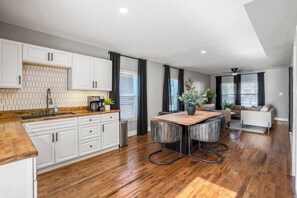 Een moderne keuken met witte kasten, een houten aanrecht en een centraal eiland met barkrukken.