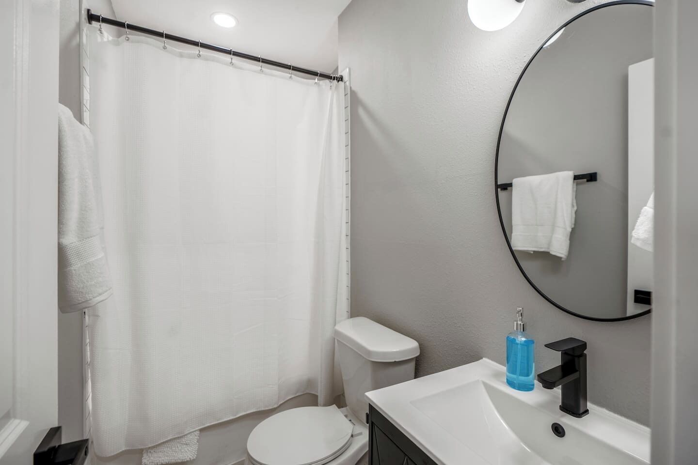 A bathroom with a shower curtain, toilet, sink, and mirror.