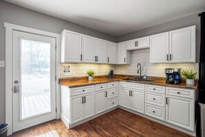 Een keuken met witte kastjes, een houten aanrecht, een spoelbak en een koffiezetapparaat.