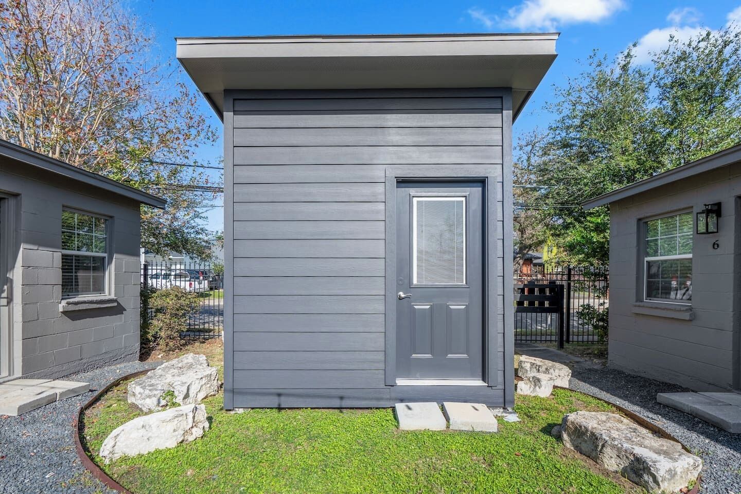 A small, single-story building with a gray exterior, a front door with a window, and a number '6' on the side.