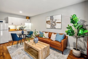 A modern living room with a wooden coffee table, a sofa with cushions, a dining table with chairs, a kitchen area with cabinets, and a potted plant. - Stylish Studio minutes from Downtown, near top attractions with easy parking and self check-in (Houston)