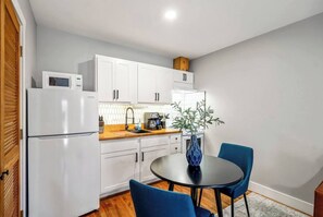 A compact kitchen with white cabinets, a microwave, a coffee maker, and a dining table with blue chairs. - Stylish Studio minutes from Downtown, near top attractions with easy parking and self check-in (Houston)
