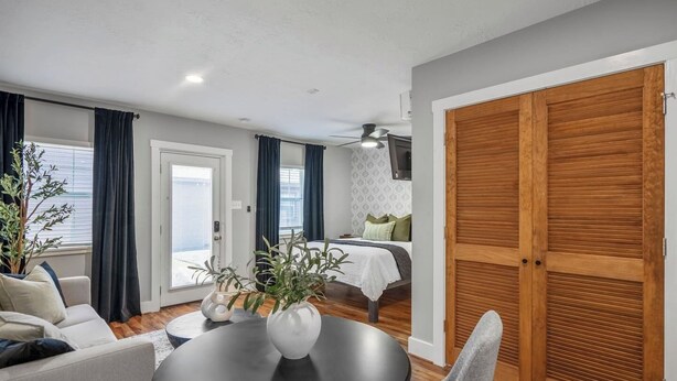 Una sala de estar moderna con sofá, una mesa de comedor con sillas, un amplio guardarropa de madera y una cama con cabecera estampada.