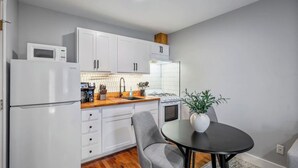 Una cocina compacta con gabinetes blancos, microondas, estufa y comedor con mesa y sillas.