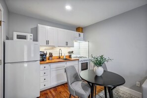 A compact kitchen with white cabinets, a microwave, a stove, and a dining area with a table and chairs. - Comfortable Houston hideaway near Downtown and attractions with fast WiFi, parking (Houston)