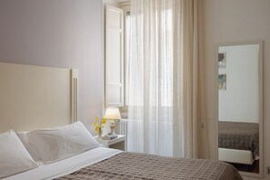 Ein Hotelzimmer mit einem Bett, einem Nachttisch mit Lampe, einem Spiegel und transparenten Vorhängen.