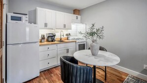 Une cuisine compacte avec des meubles blancs, une machine à café, un four à micro-ondes et un coin repas comprenant une table et des chaises.