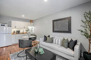 A modern living room with a sofa, coffee table, and a dining area with a kitchen in the background. - Private gated studio near Downtown Houston, Med Center & NRG with fast WiFi and parking (Houston)