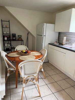 A kitchen with white cabinets, a white refrigerator, a dining table with woven placemats, wicker chairs, and a coffee machine. - Cozy 2-bedroom apartment in quaint South Amboy with AC (South Amboy)