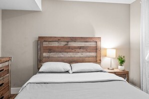 Un letto con una testiera in legno, una lampada da comodino e una pianta in vaso.