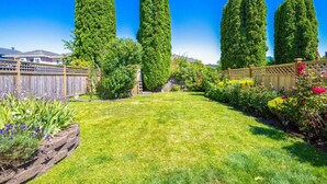 Un jardin bien entretenu avec une pelouse, de grands arbres, une clôture en bois et diverses plantes.
