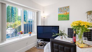 Une pièce dotée d’une grande fenêtre, d’un téléviseur à écran plat, d’une table à manger avec des chaises et d’un tableau accroché au mur.