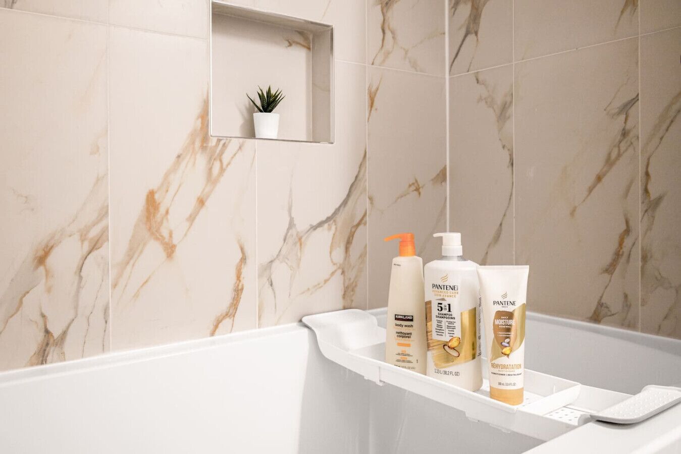 A bathroom with marble tiles, a small plant on a shelf, and toiletries on a counter.