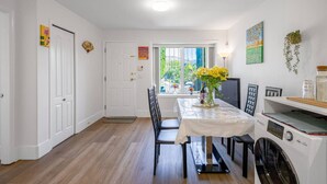 Un espace repas comprenant une table, des chaises, un lave-linge et une fenêtre donnant sur un paysage verdoyant.