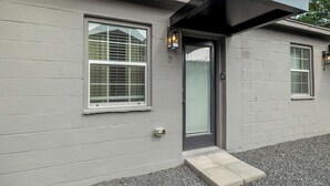 Un bâtiment moderne à la façade grise, doté d’une porte avec un panneau de verre et d’une petite marche menant à l’entrée.