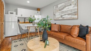 Un salon moderne avec un canapé en cuir marron, une table basse ronde et un coin repas comprenant une table et des chaises blanches.