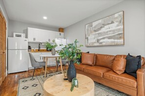 A modern living room with a brown leather sofa, a round coffee table, and a dining area with a white table and chairs. - Central Houston Studio Near EaDo and Downtown (Houston)