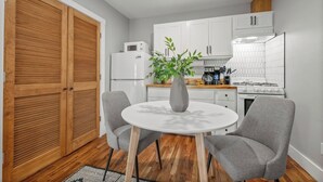 Une cuisine compacte comprenant une table ronde, deux chaises, un réfrigérateur, un four à micro-ondes, une cuisinière et une plante en pot.