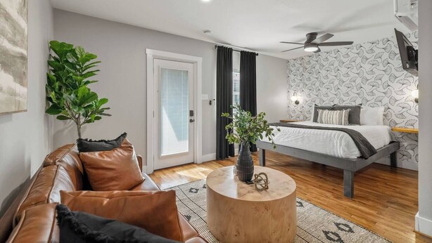 Une chambre moderne avec un lit, un ventilateur de plafond, une grande fenêtre avec des rideaux, une table basse en bois et une plante en pot.