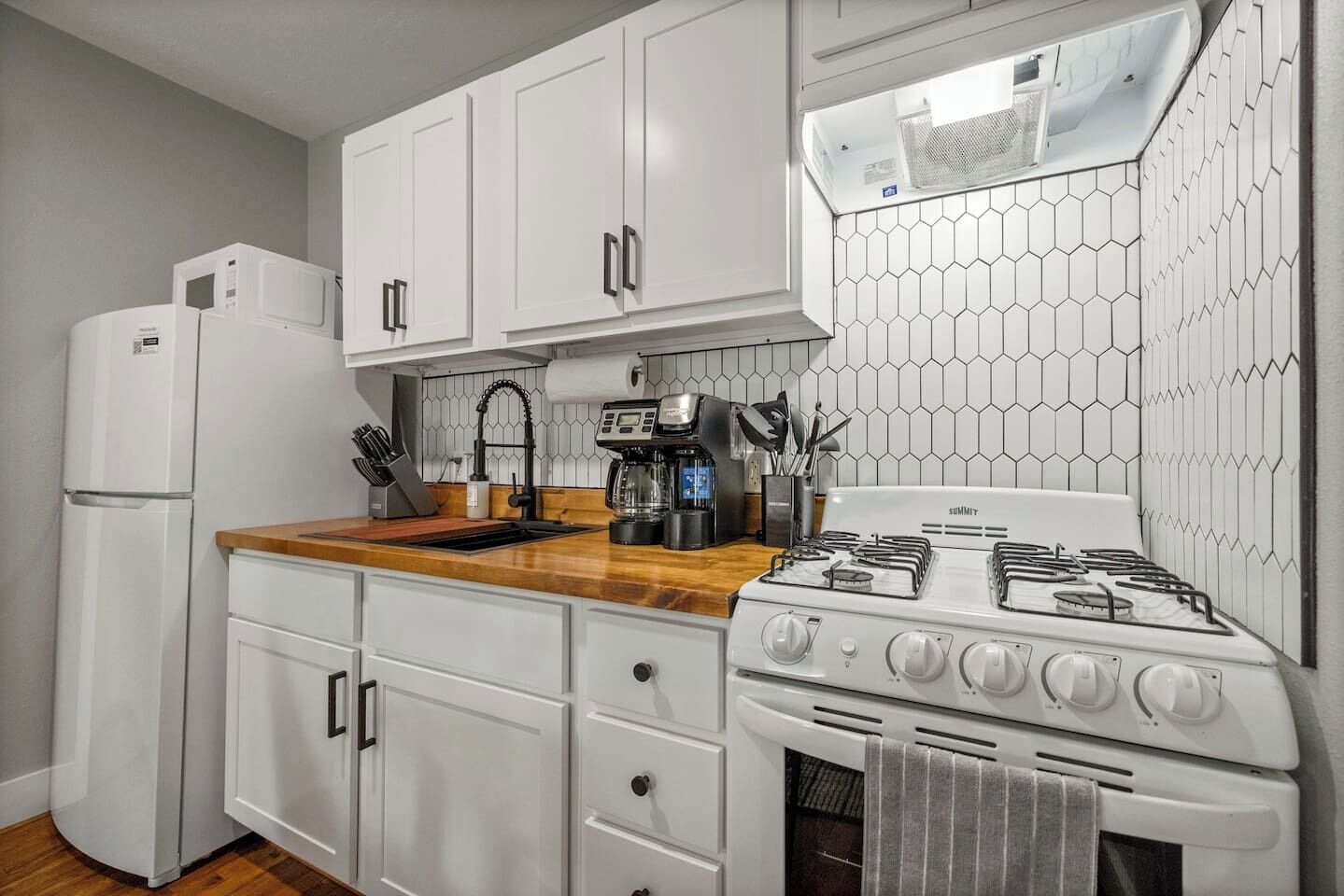 A kitchen with white cabinets, a wooden countertop, a stove, a refrigerator, and a coffee maker.