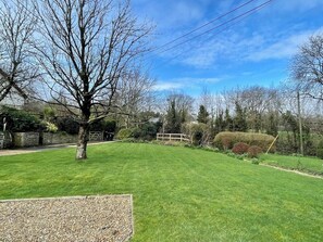 A well-maintained lawn with a single tree, a stone wall, and a wooden fence in a residential setting. - Alma Cottage - 3 minute walk to Studland beach, garden, parking 3 bedrooms (Studland)