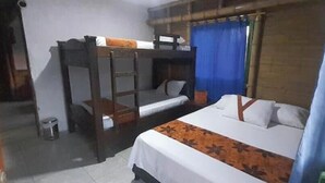 Une chambre avec des lits superposés, un lit simple, une petite poubelle et une fenêtre avec des rideaux bleus.