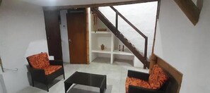 Una stanza con due divani, un tavolino da caffè, una porta in legno e una scala.