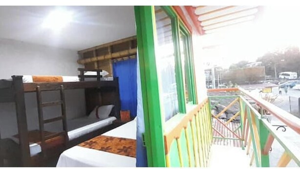 Une chambre avec des lits superposés, une fenêtre donnant sur la rue et un balcon avec des balustrades.