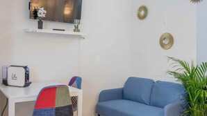 A room with a flat-screen TV, a small table with a toaster, a blue sofa, and decorative wall art. - Small studio downtown (Orléans)