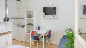 A compact living space with a kitchenette, a dining area with two chairs, a TV mounted on the wall, and a potted plant. - Small studio downtown (Orléans)