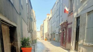 A cobblestone street with buildings on either side, a large orange planter with greenery, and a clear blue sky. - Small studio downtown (Orléans)