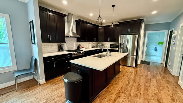A modern kitchen with dark cabinets, a stainless steel refrigerator, and a large island with a sink. - Luxe Modern Farmhouse in the heart of everything! (Atlanta)