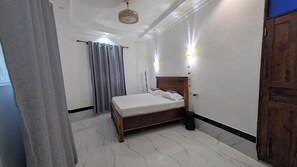 Une chambre à coucher avec un lit, des rideaux, une porte en bois et un luminaire au plafond.