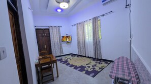 Une pièce avec une porte en bois, un téléviseur fixé au mur, un tapis à motifs et un lit recouvert d’une couverture à carreaux.