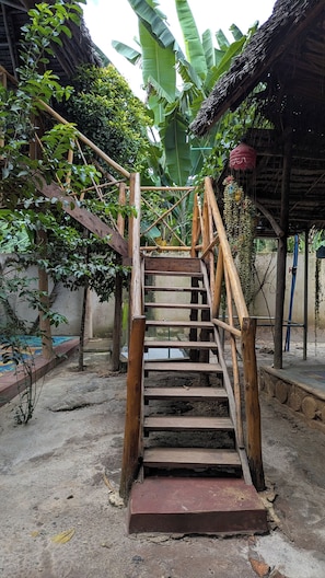 A wooden staircase leading to a thatched-roof structure surrounded by lush greenery. - Zan Culinary (W7F2+VM Zanzibar, Tanzania)