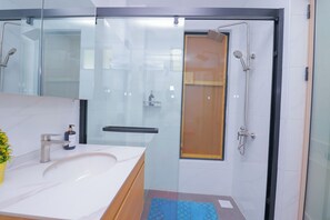 Ein modernes Badezimmer mit einer gläsernen Duschkabine, einem weißen Waschbecken und einer Holzkommode.