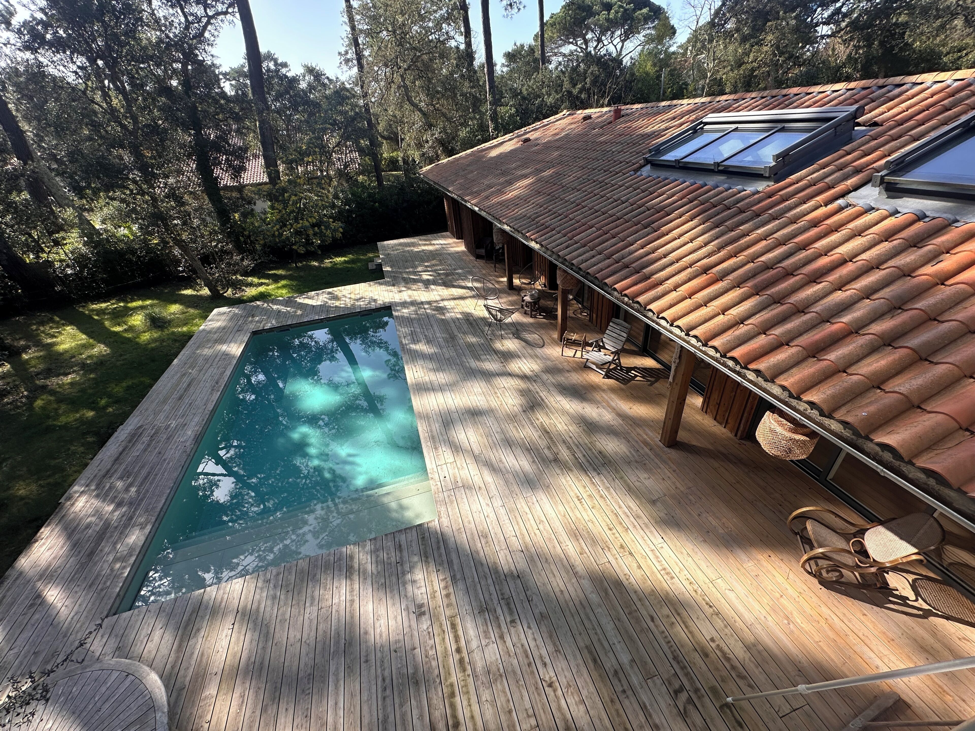 A wooden deck with a swimming pool, a covered patio area, and a tiled roof.