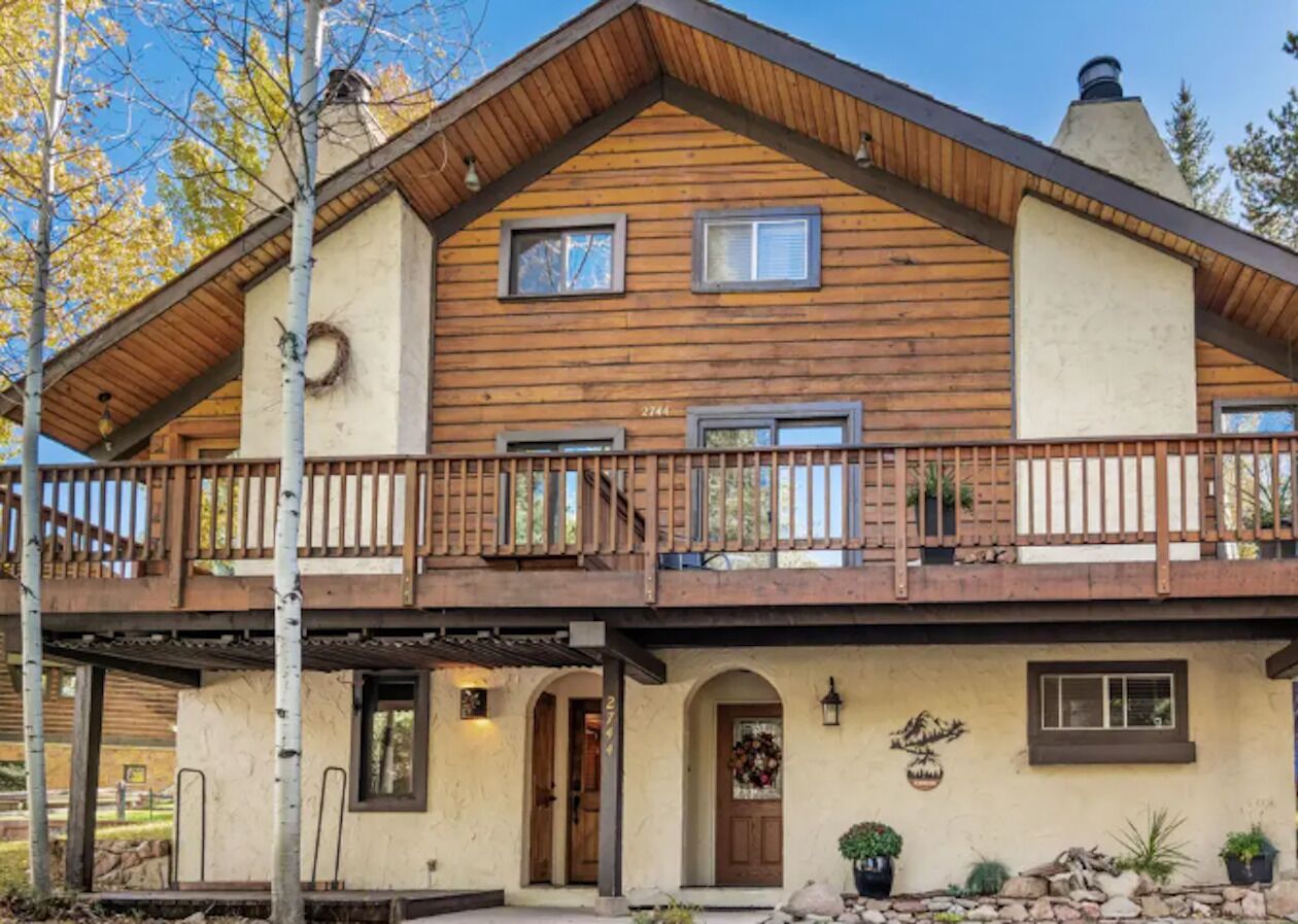 Une cabane en rondins à deux étages, dotée d’un balcon, d’une porte d’entrée et d’un petit porche.