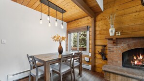 A wooden interior with a dining table, chairs, a vase with flowers, a fireplace, and a window with a view of trees. - Cozy Duplex in West Vail – Near Vail Village (Vail)