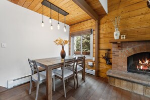 A wooden interior with a dining table, chairs, a vase with flowers, a fireplace, and a window with a view of trees. - Cozy Duplex in West Vail – Near Vail Village (Vail)