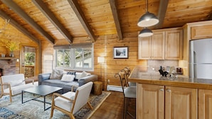 A cozy cabin interior with a wooden ceiling, a fireplace, a sofa, a dining area, and a kitchen with wooden cabinets and a refrigerator. - Cozy Duplex in West Vail – Near Vail Village (Vail)